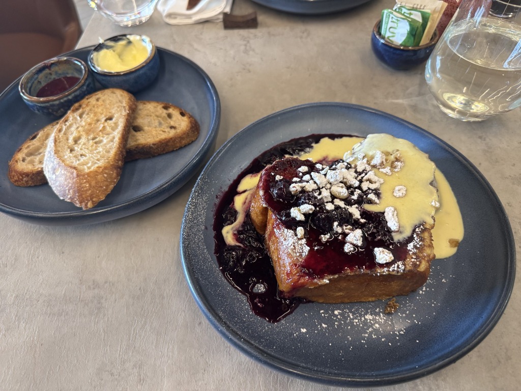 French toast topped with berry compote, powdered sugar, and vanilla sauce next to toasted bread at LB Eatery & Wine in Pembroke Pines, Florida