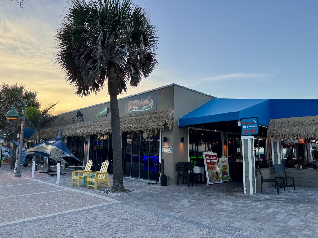 Storefront exterior of Mulligan's Beach House Bar & Grill in Vero Beach, Florida, showing a blue awning, beach chairs, and a large sailfish statue