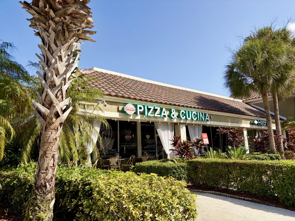 Storefront exterior of Pizza Lovers and Cucina showing Spanish tile roof, outdoor greenery, and palm trees in Plantation, Florida
